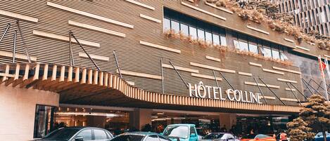 A hotel with a modern facade, multiple cars parked in front, and a visible sign reading "HOTEL COLLINE".