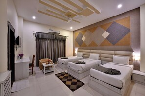 Two single beds with white linens, a seating area, and a large window with curtains.