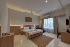Una habitación de hotel moderna con una cama grande, mesitas de noche, un escritorio, una silla, un ventilador de techo y una ventana con cortinas.