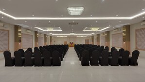 Une salle de conférence avec des rangées de chaises, un pupitre et un lustre.