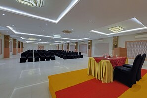 Une salle de conférence avec des rangées de chaises, une table recouverte d’une nappe rouge et un tapis jaune.