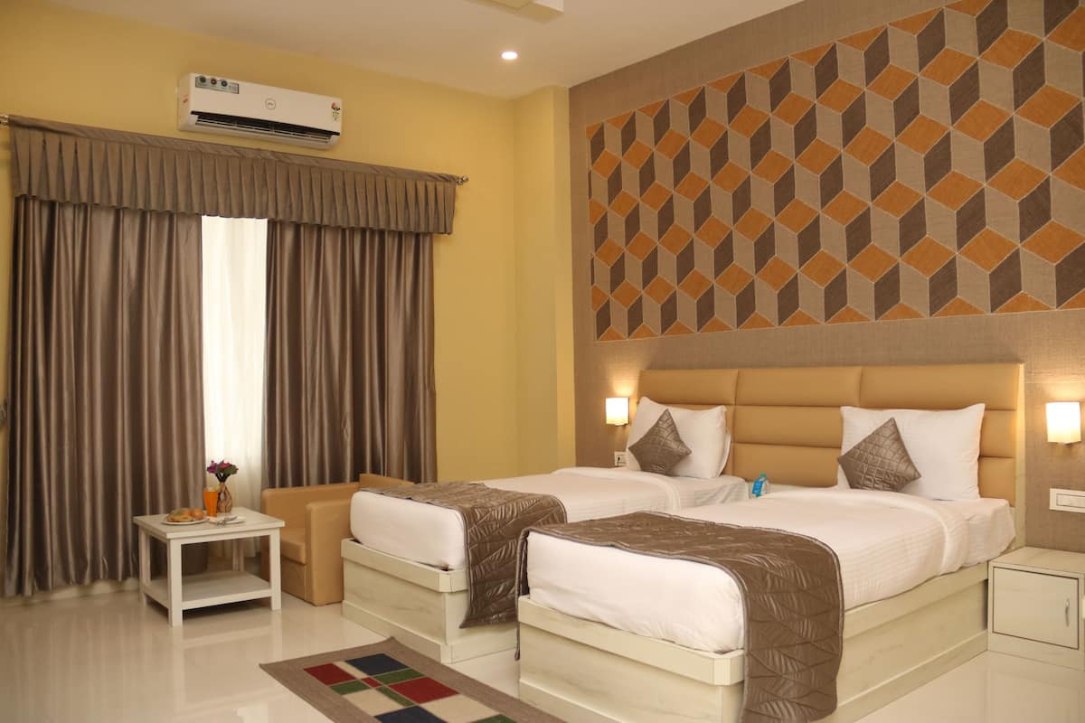 Habitación de hotel con dos camas, una mesita con un florero y fruta, y una pared con diseño.