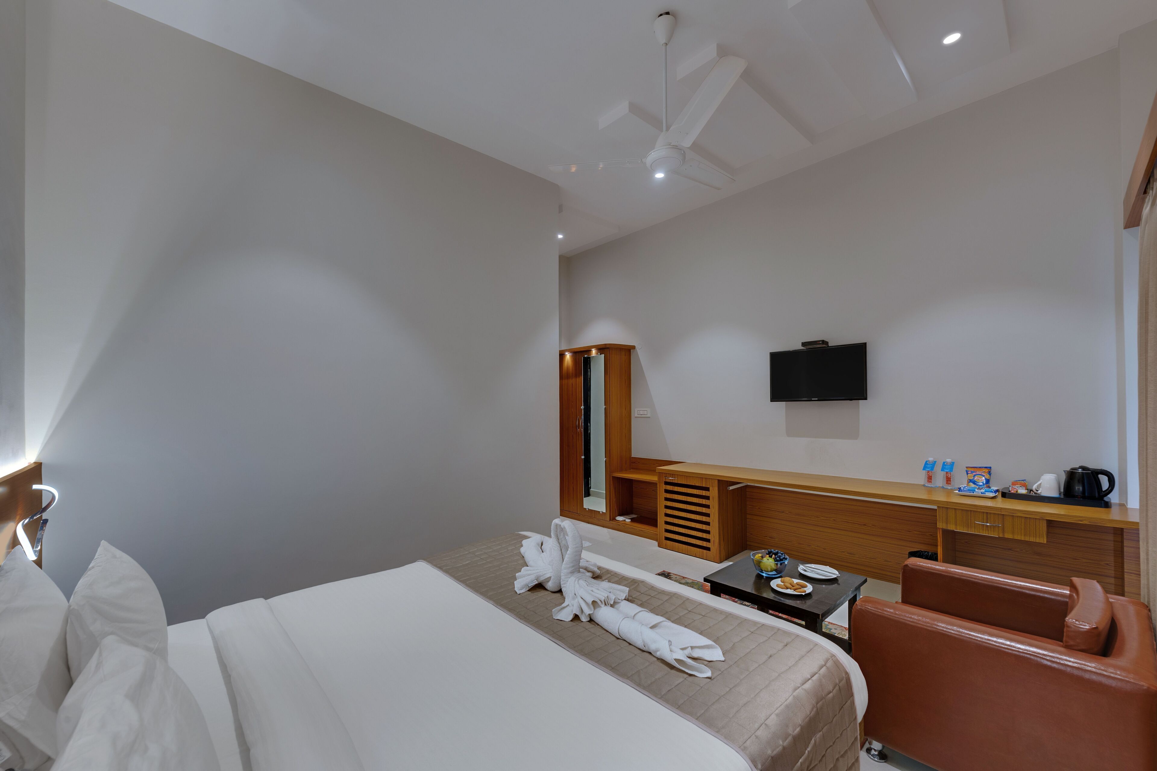 Habitación de hotel con una cama, un escritorio con televisor, una silla y una mesita con un frutero.