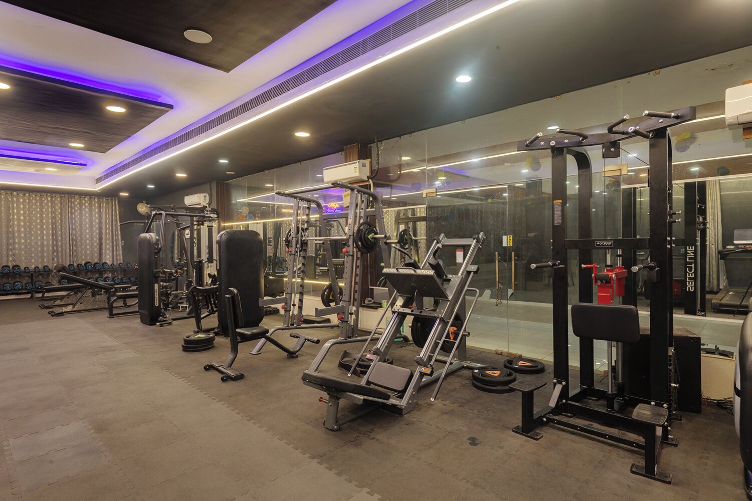A gym with various exercise equipment, including weight machines and free weights, arranged in a spacious layout.