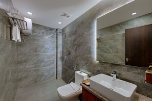 A modern bathroom with a glass shower enclosure, a toilet, a sink with a countertop, and a large mirror. - GenX Mirzapur (Mirzapur)