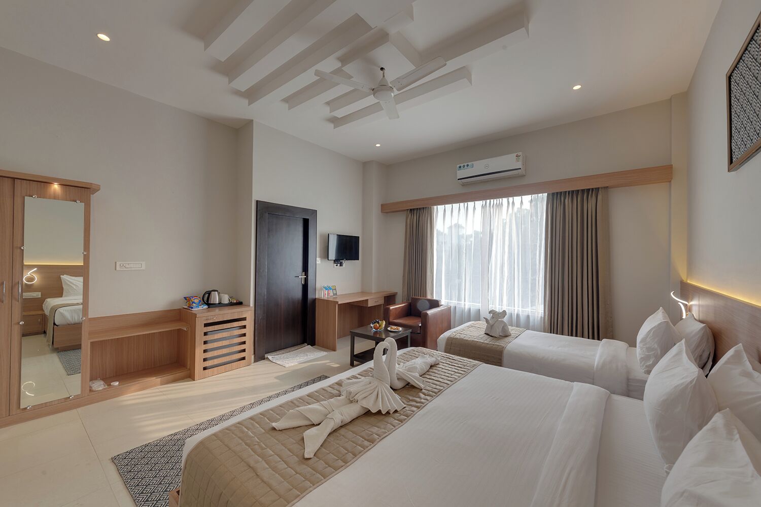 A hotel room with two beds, a desk, a chair, a TV, and a window with curtains.