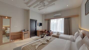 A hotel room with two beds, a desk, a chair, a TV, and a window with curtains.