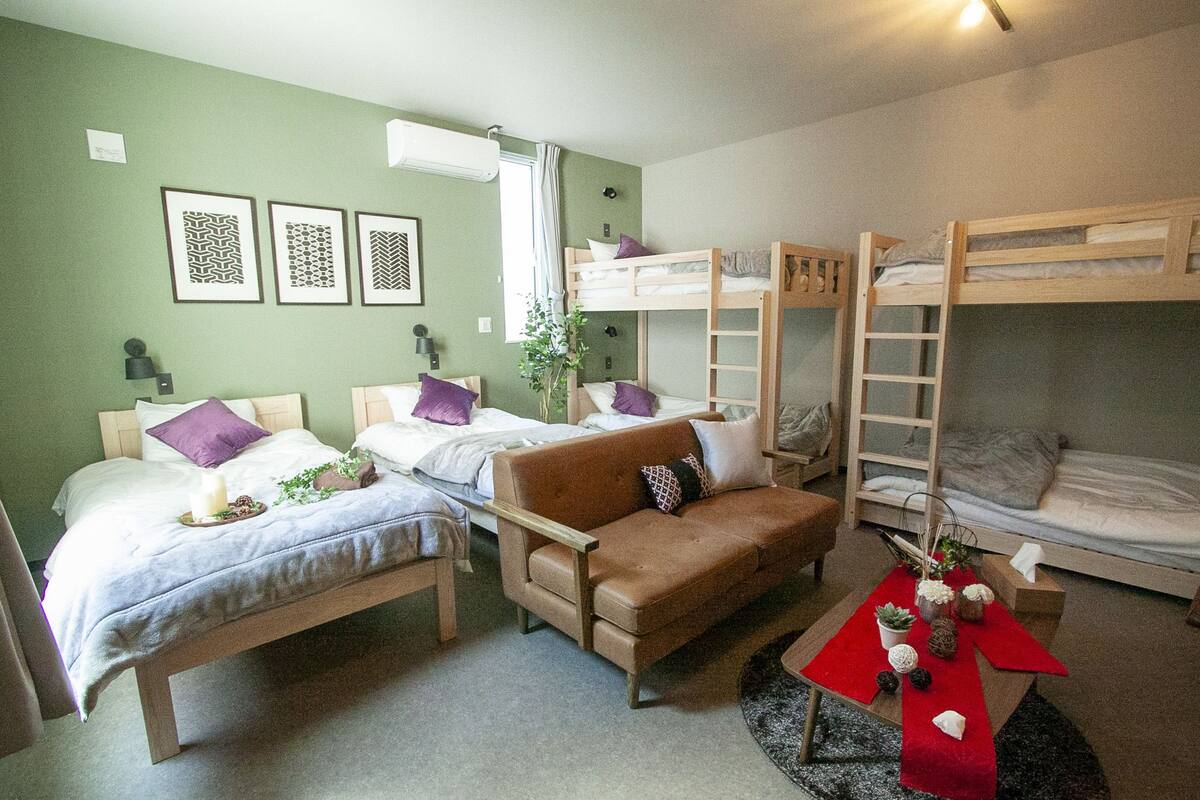 Une chambre avec deux lits simples, un canapé, des lits superposés, une petite table agrémentée d’objets décoratifs et des œuvres d’art encadrées accrochées au mur.
