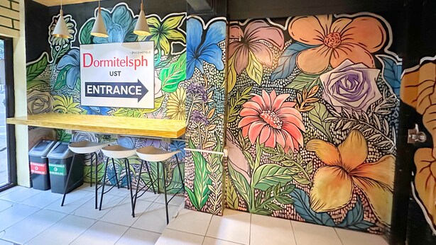 A colorful mural with floral patterns and a sign indicating the entrance to Dormitelsph. - Dormitelsph UST (Manila)