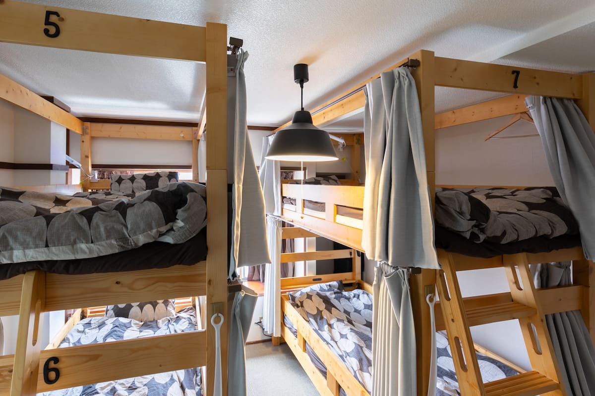 A dormitory-style room with bunk beds, wooden beams, and a hanging light fixture.