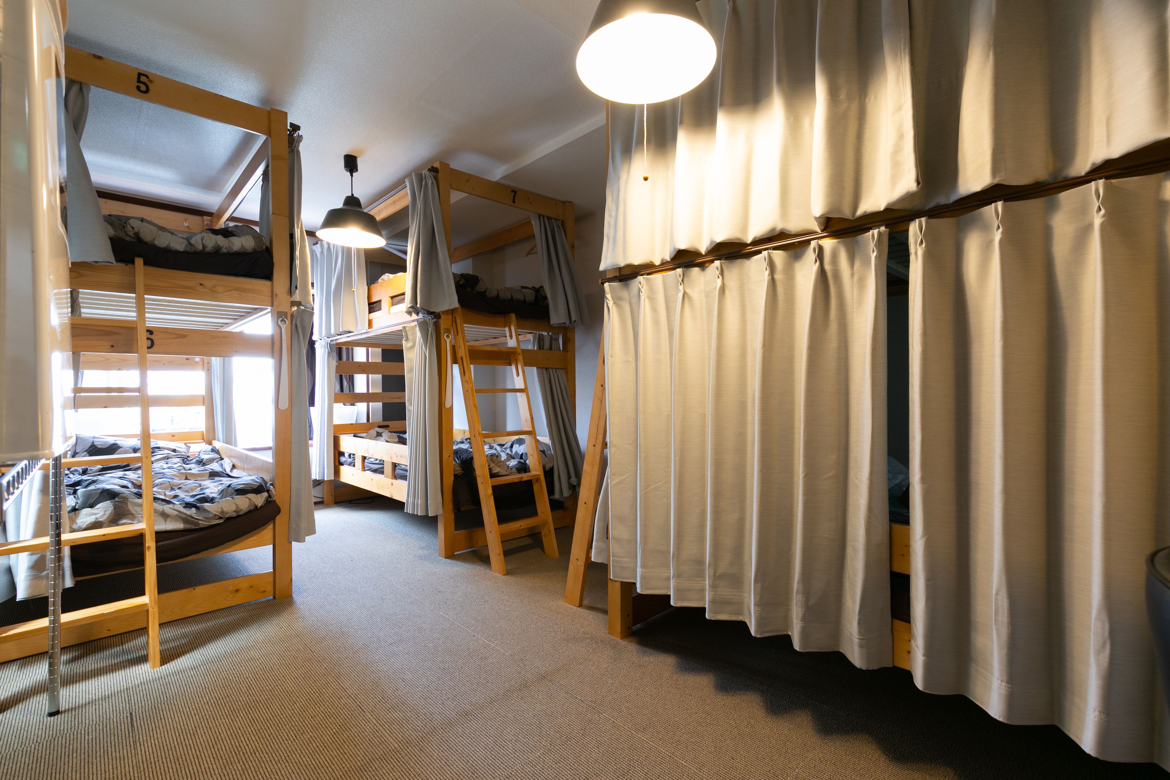 A dormitory room with bunk beds, a ladder, a desk, and a hanging light fixture.