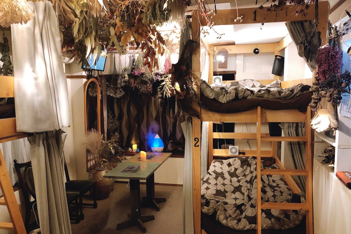 A cozy room with a bunk bed, a small table with candles, and a variety of plants and decorations.