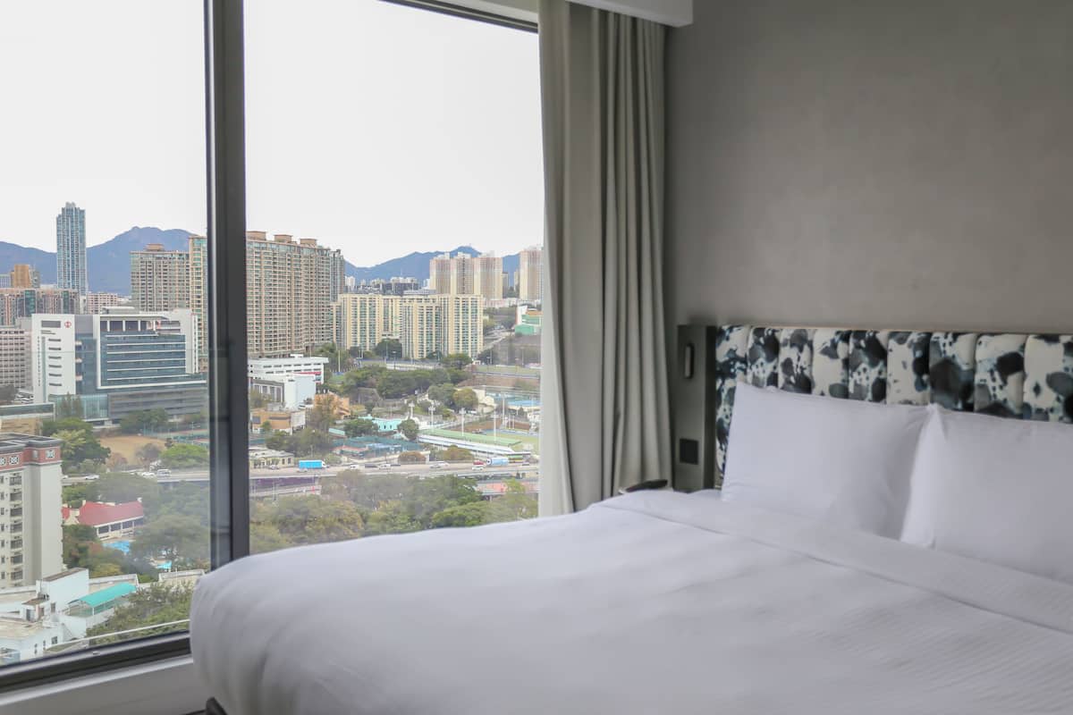 Habitación de hotel con una cama grande, vista a la ciudad y cortinas en la ventana.
