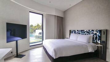 A modern hotel room with a large bed, a flat-screen TV, and a view of the outdoors through a large window.
