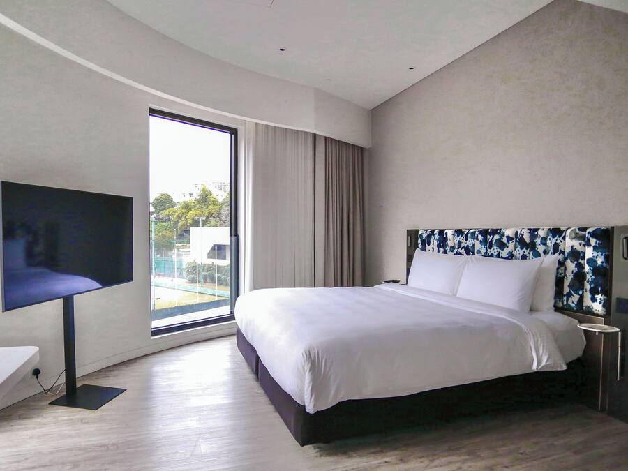A modern hotel room with a large bed, a flat-screen TV, and a view of the outdoors through a large window.