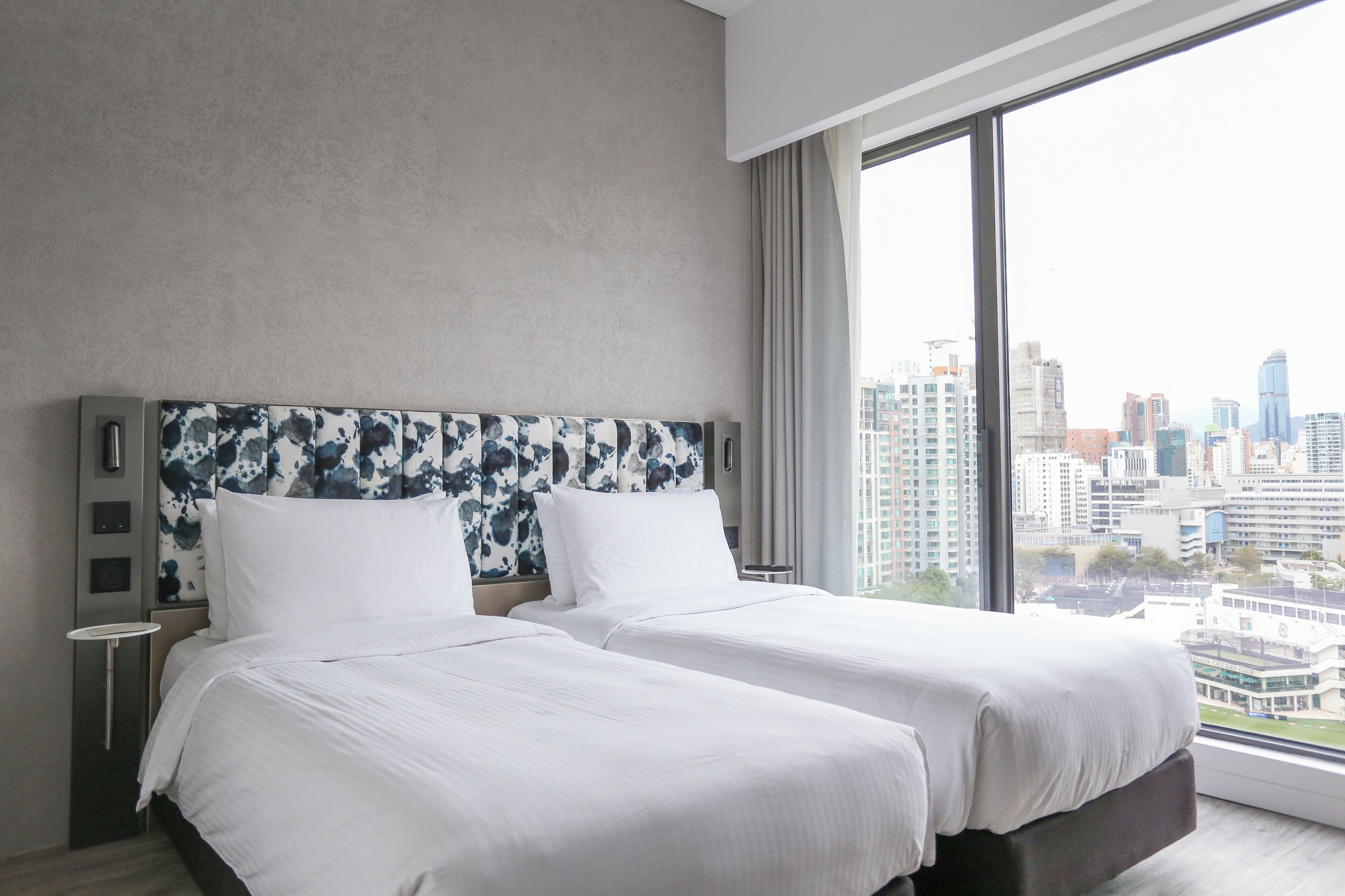 Una habitación de hotel moderna con dos camas, vistas a la ciudad y un ventanal amplio.