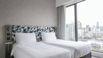 Una habitación de hotel moderna con dos camas, vistas a la ciudad y un ventanal amplio.