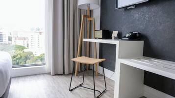 A modern hotel room with a desk, chair, and a large window offering a city view.