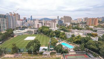 An aerial view of a cityscape with a large open green space, possibly a park, surrounded by high-rise buildings and a construction crane in the distance.