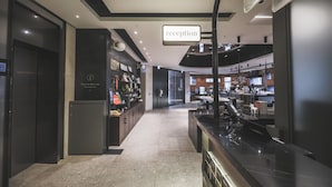 A modern reception area with a 'reception' sign, a check-in counter, and a view into the hotel's interior.