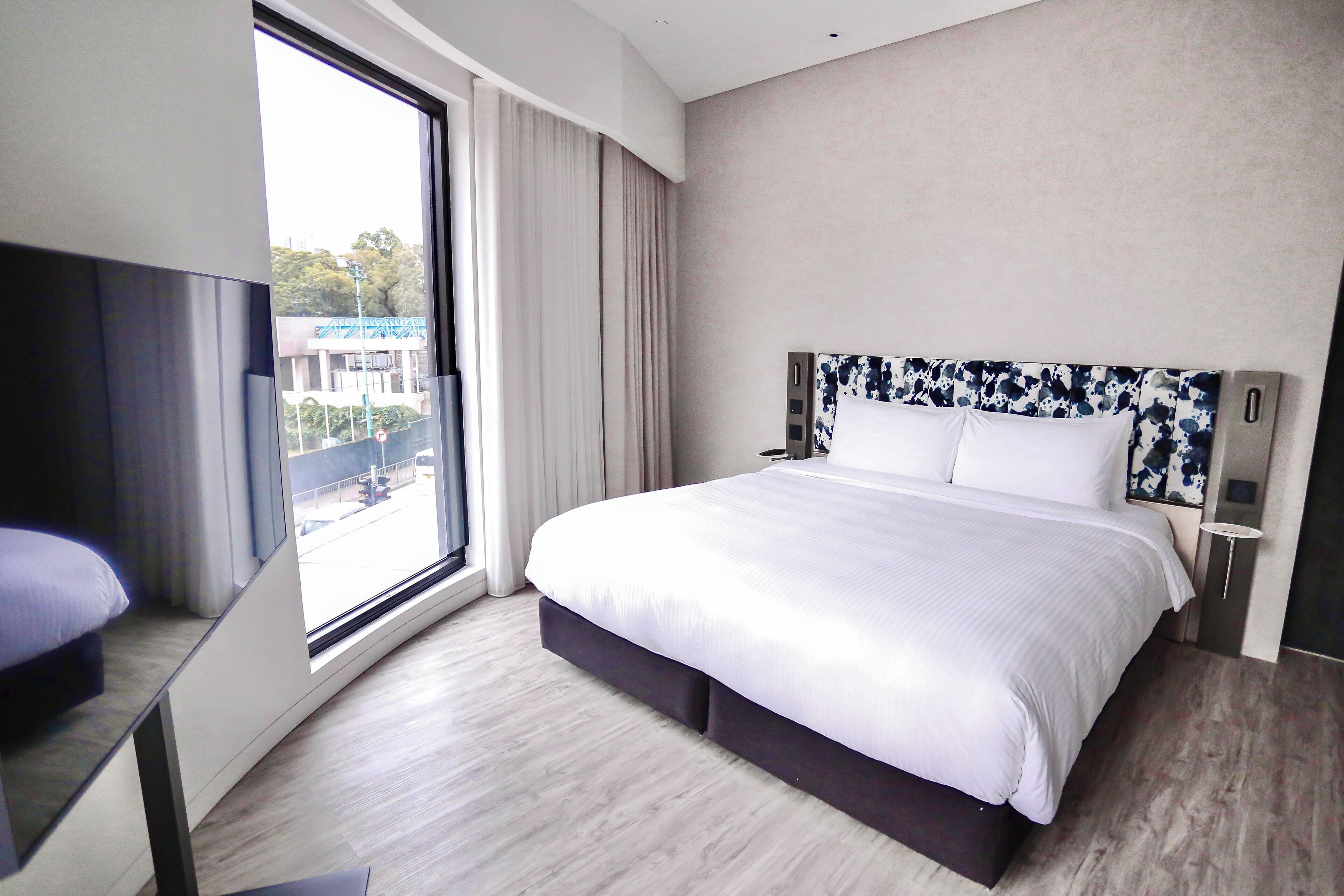 A modern hotel room with a large bed, a TV, and a view of the city through the window.