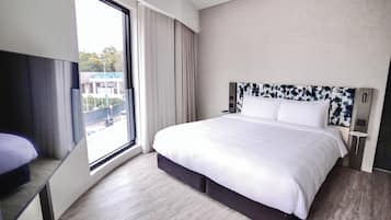 A modern hotel room with a large bed, a TV, and a view of the city through the window.