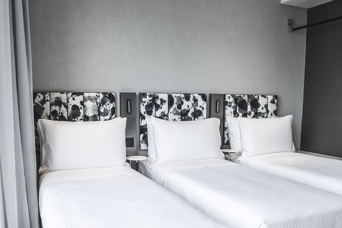 Habitación de hotel con dos camas, cada una con ropa blanca y cabeceros con un diseño abstracto en blanco y negro.
