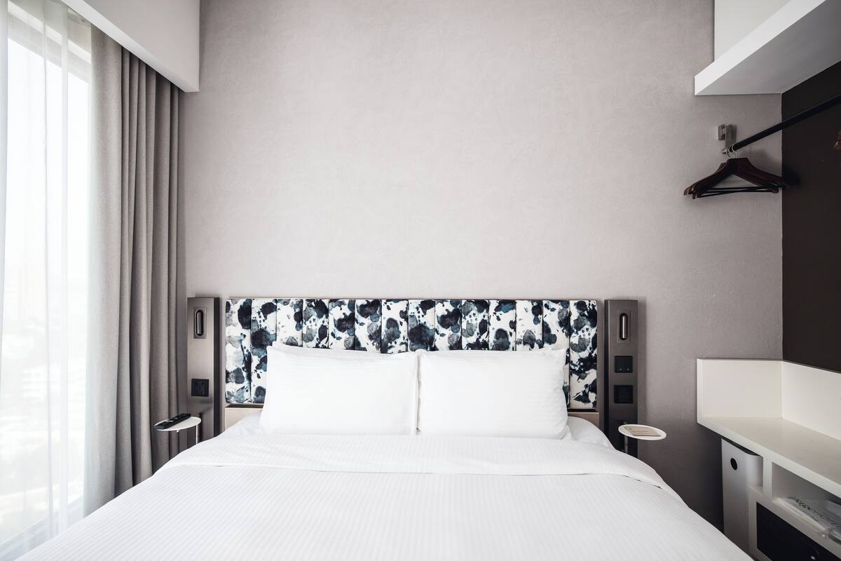 Una habitación de hotel moderna con una cama grande, una mesita de noche, un escritorio pequeño y un perchero.