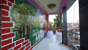 A balcony with a mural, white tables, and chairs, overlooking a cityscape. - Hotel Anand Lok (Rajgir)