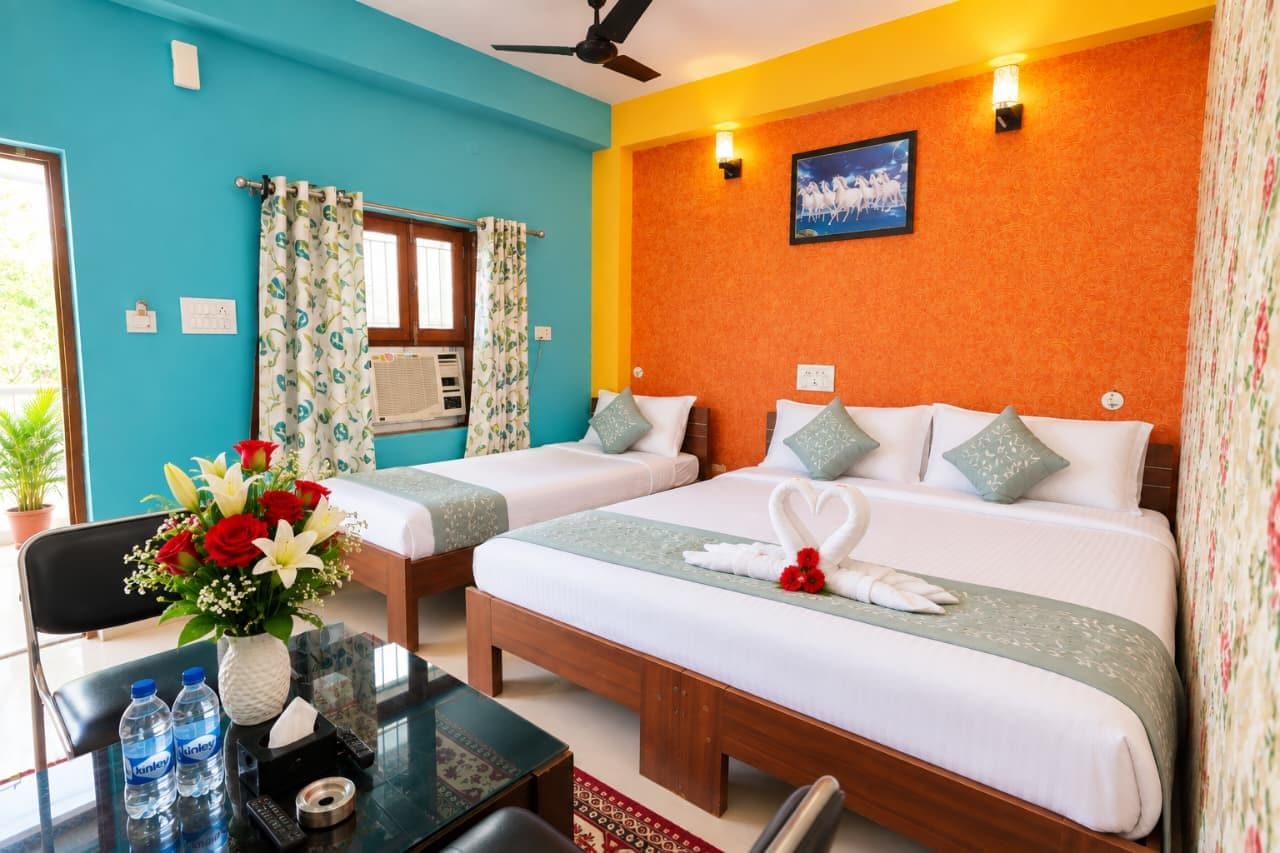 A hotel room with two beds, a desk with a chair, a vase of flowers, and a ceiling fan.