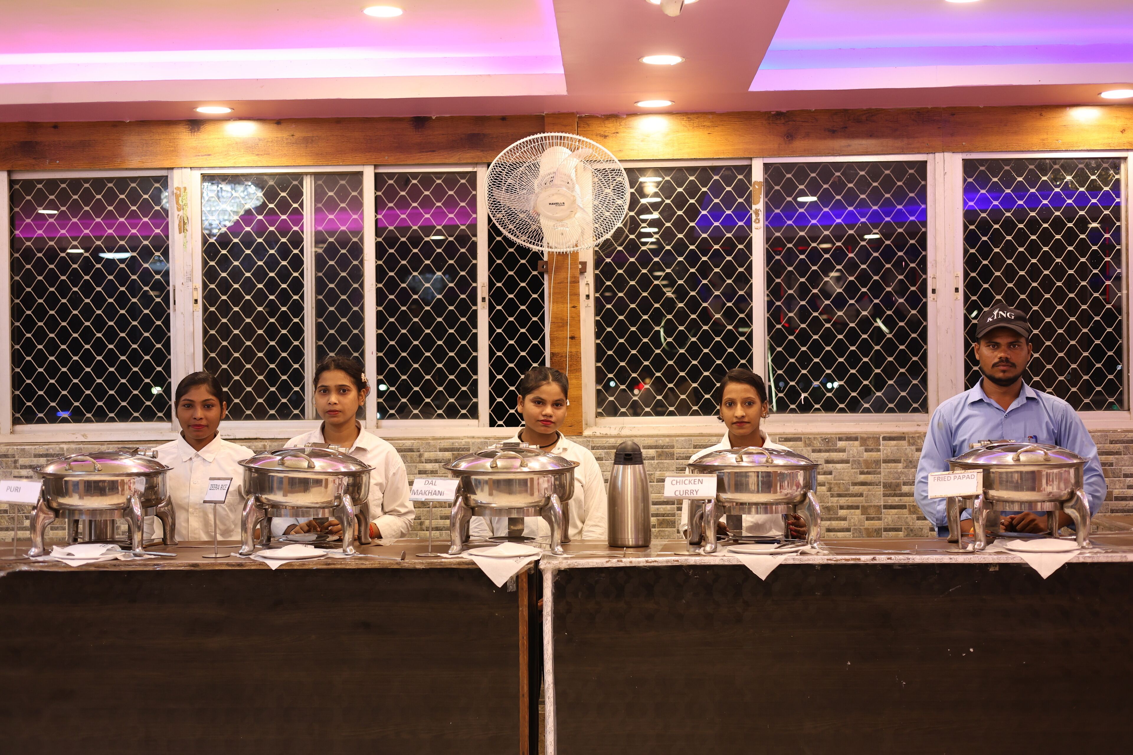 A buffet setup with labeled dishes and a fan in the center.