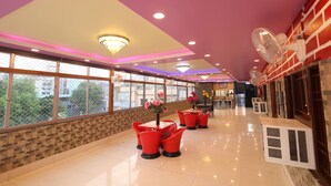A spacious indoor area with a high ceiling, large windows, and red chairs. - Hotel Anand Lok (Rajgir)