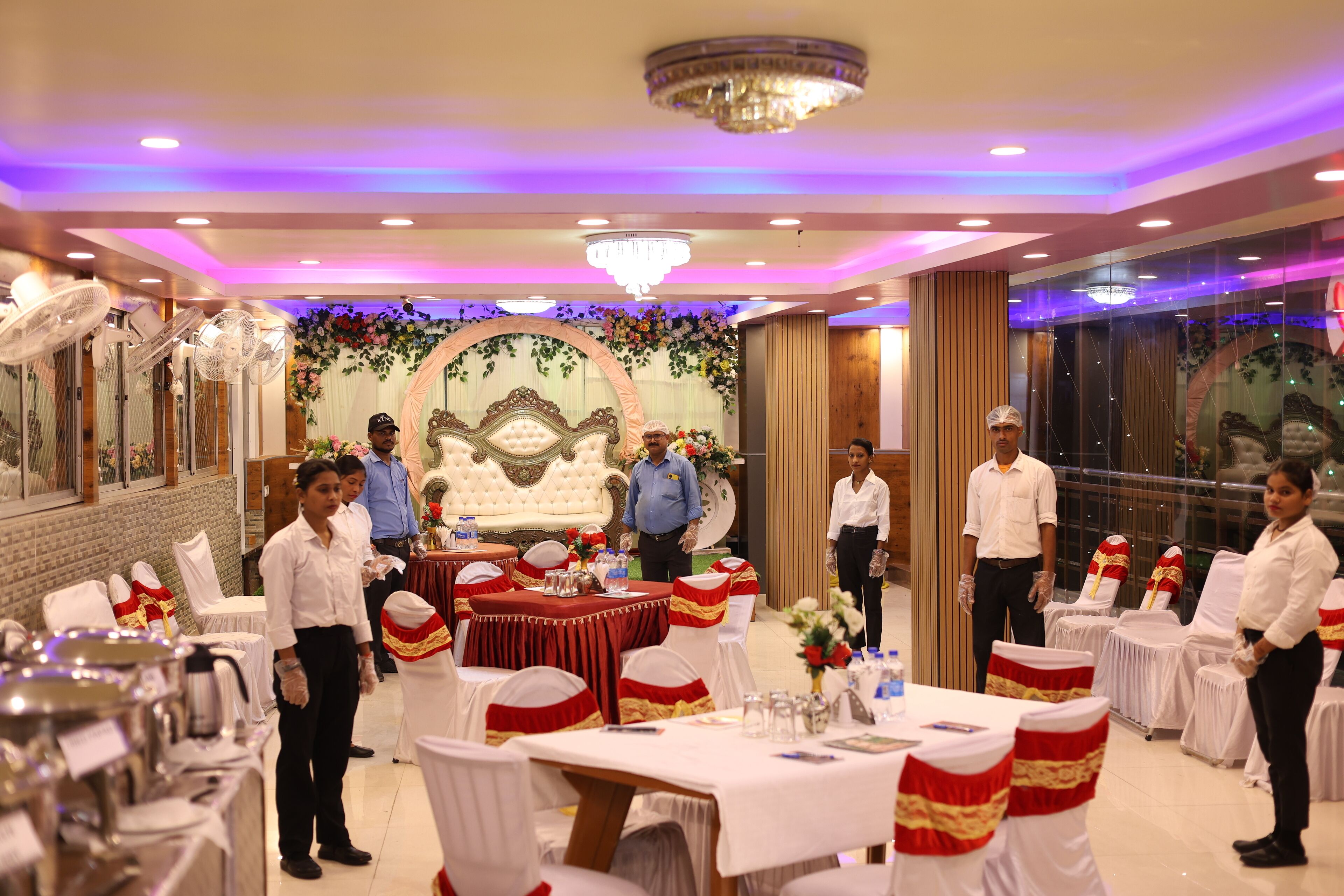 A banquet hall with round tables, white chairs, and a stage with floral decorations.