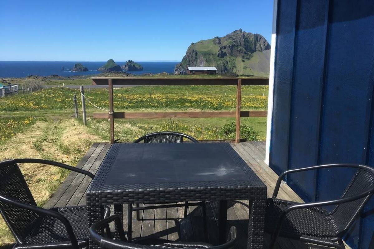 Un balcón con vista al océano y una montaña, con una mesa y sillas.