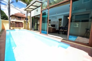 A modern house with a swimming pool, large glass doors leading to a living area, and a visible staircase. - Baan Aroonpat (Patong)