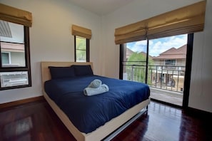 A bedroom with a large bed, two windows with curtains, and a balcony with a view of houses. - Baan Aroonpat (Patong)