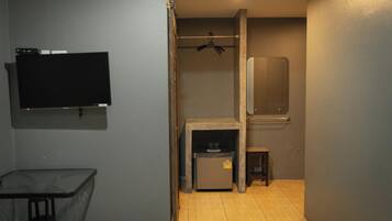 Habitació compacta amb televisió de pantalla plana penjada a la paret, una taula petita, un refrigerador i una banca de fusta.