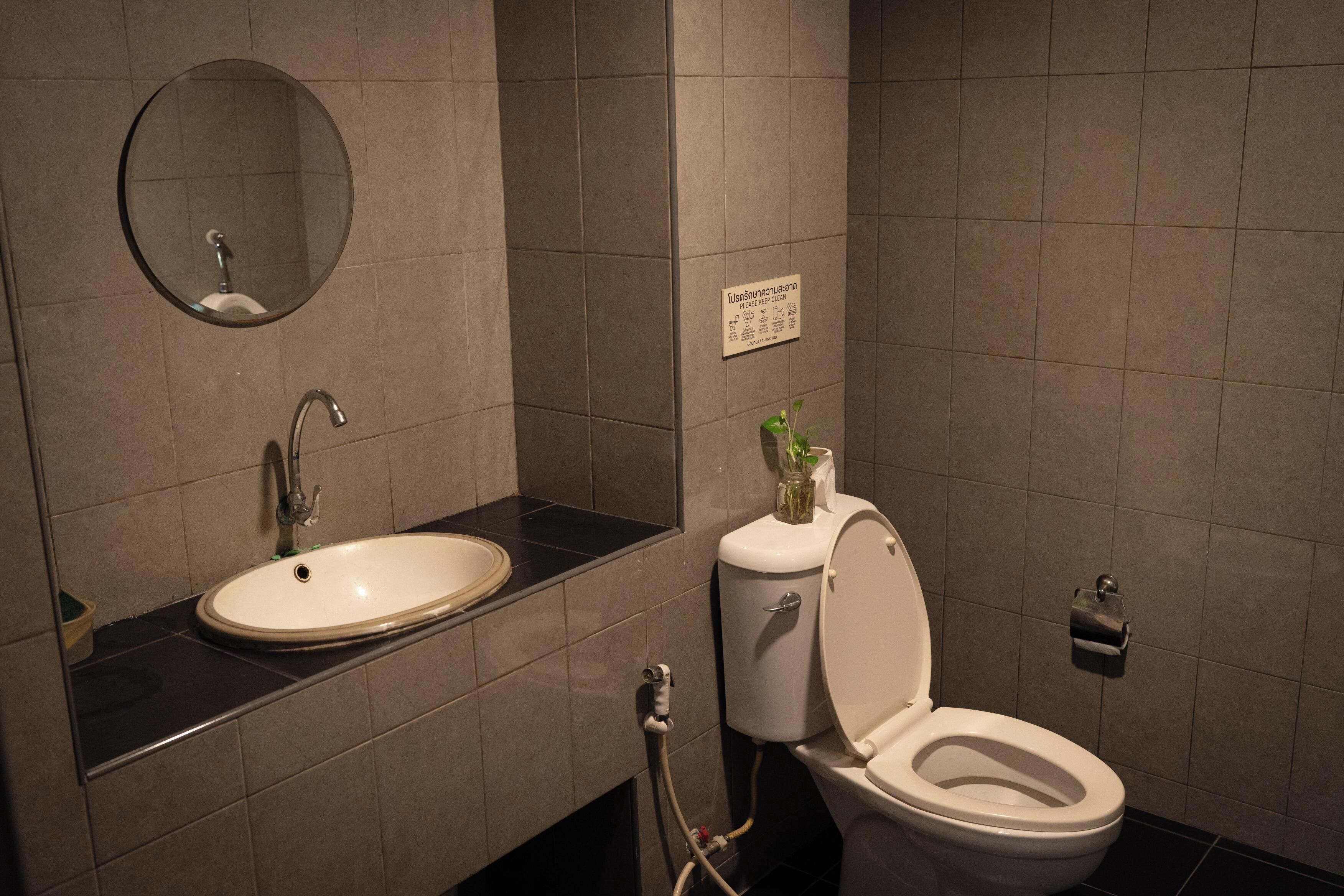 A bathroom with a sink, mirror, toilet, and a sign on the wall.