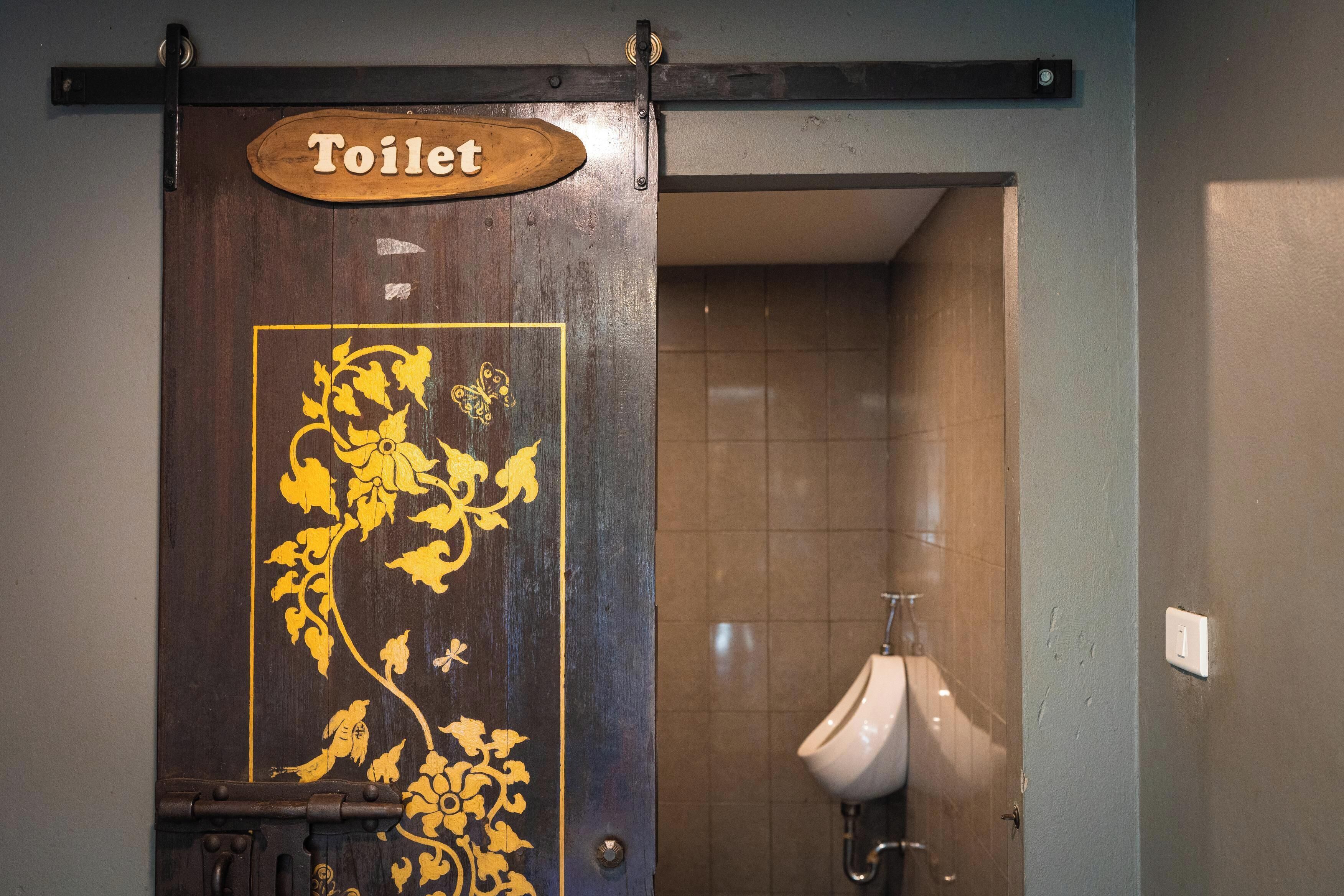 Eine Holztür mit Toilettensymbol und einem dekorativen Blumenmuster.