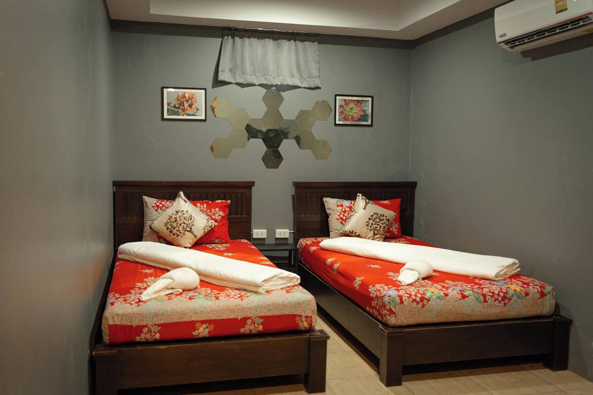 Un dormitorio con dos camas, cada una con ropa de cama y almohadas estampadas con motivos florales, un adorno en la pared y un equipo de aire acondicionado.
