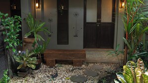 Un patio con un banco de madera, plantas en macetas, una puerta con ventana y elementos decorativos en la pared.