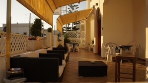 A covered outdoor seating area with white plastic chairs and tables, a small pool, and a wooden bench. - Albergo 2 Mari (Castrignano del Capo)