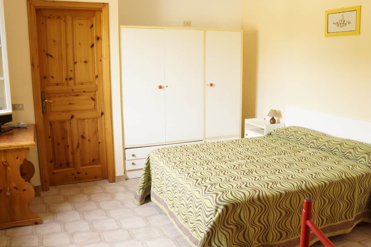 A bedroom with a bed, a wardrobe, a desk, and a chair.