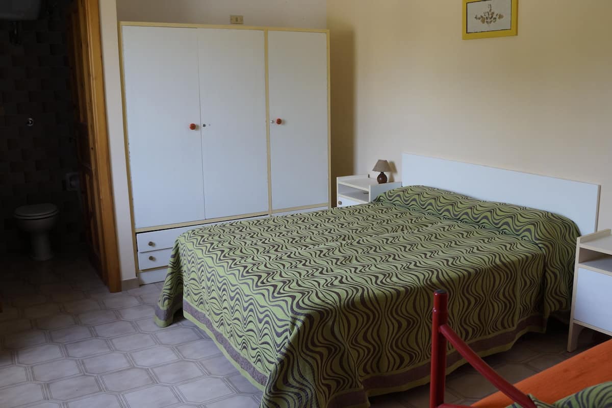 A bedroom with a bed, a nightstand, a wardrobe, and a toilet.