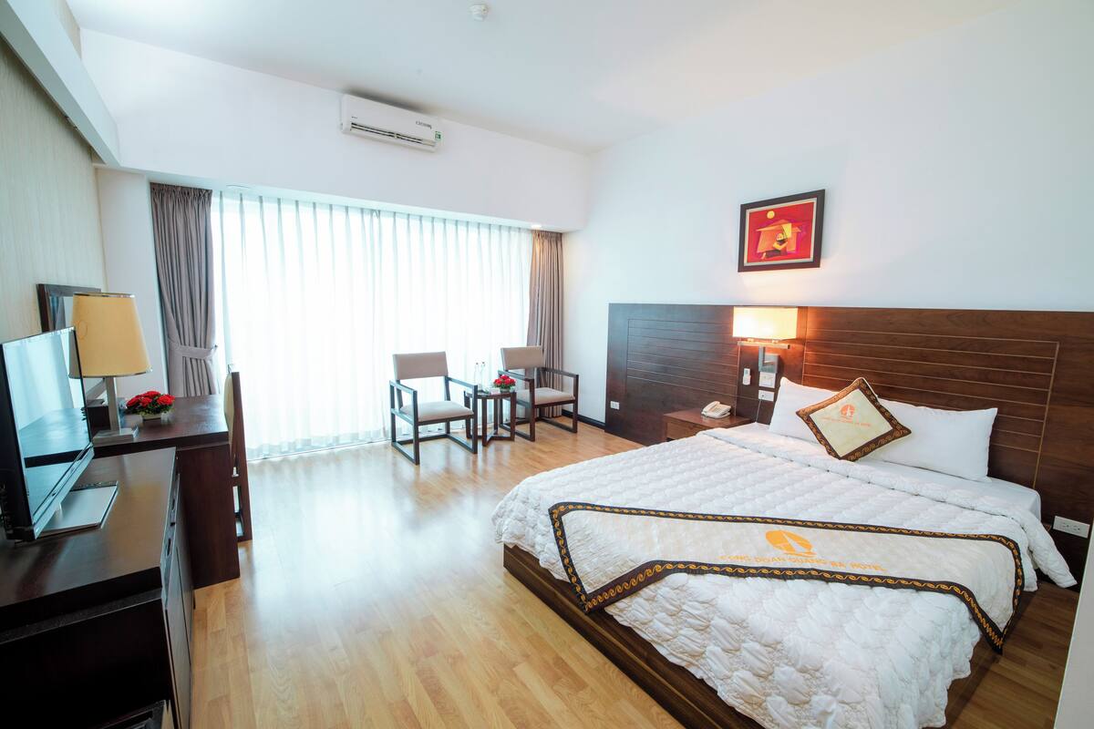 A hotel room with a bed, desk, chairs, and a window with curtains.