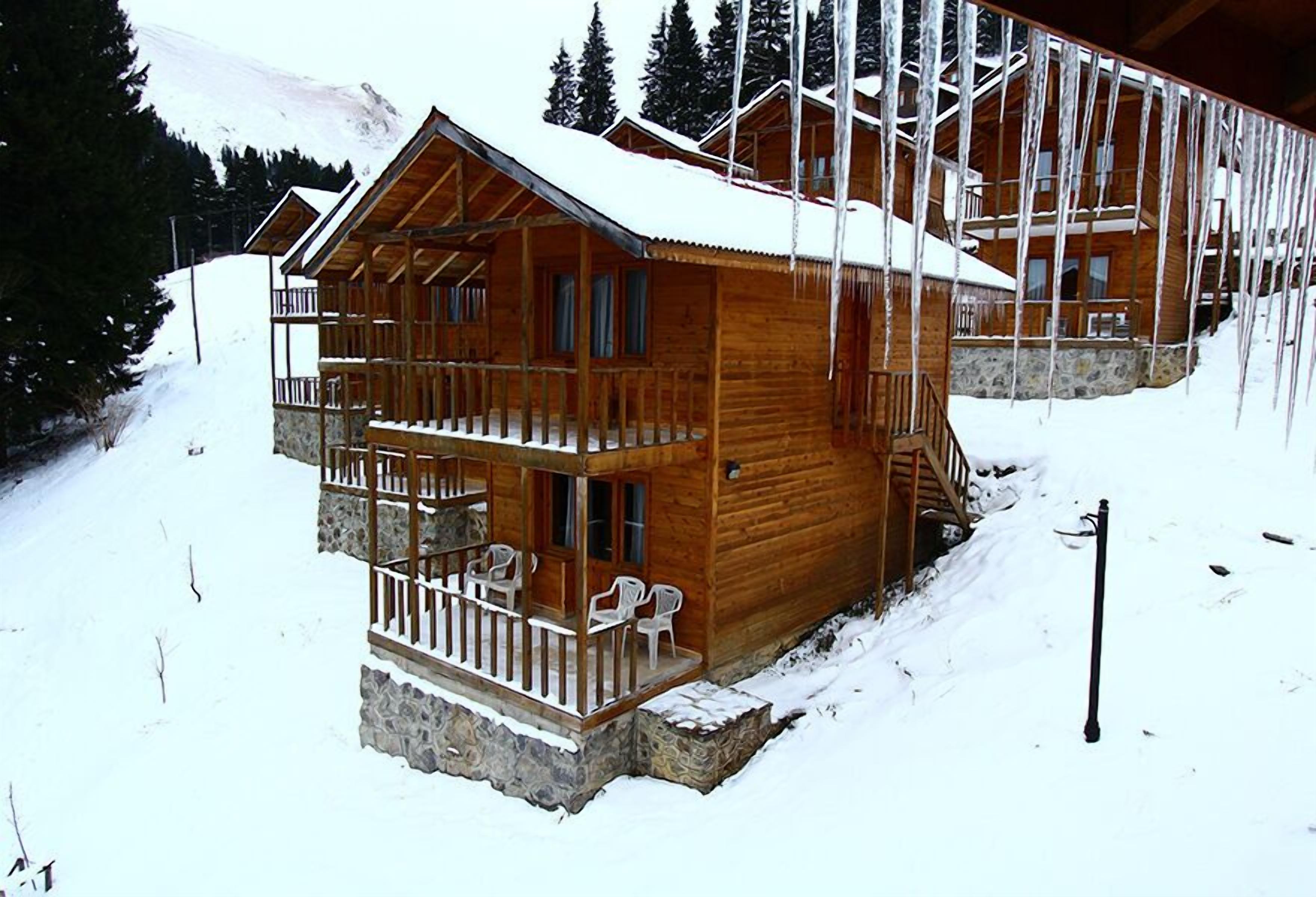 A wooden cabin with a balcony and stone foundation, surrounded by snow and trees.