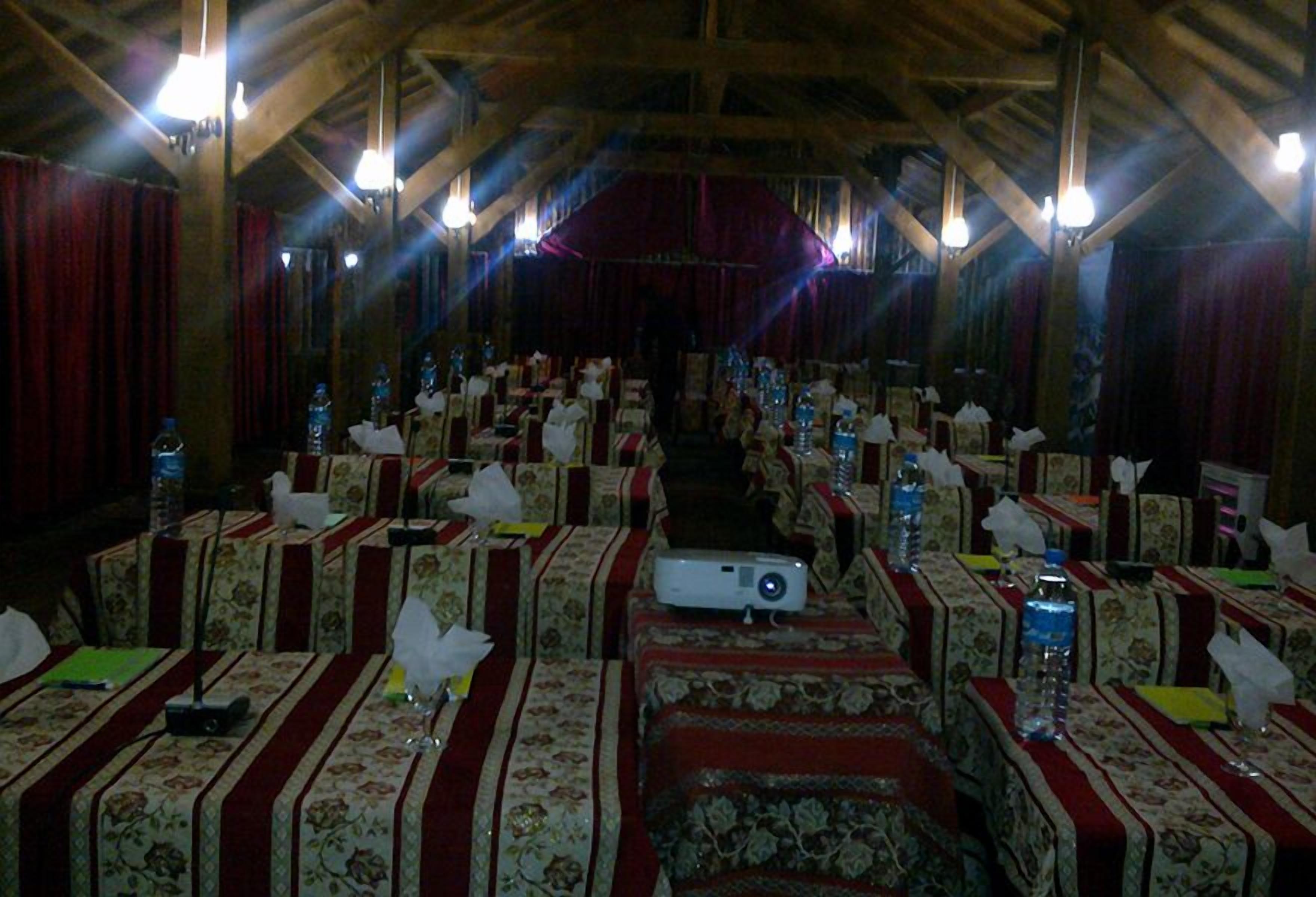 Un salón de banquetes con filas de mesas, cada una con manteles florales y cortinas rojas.