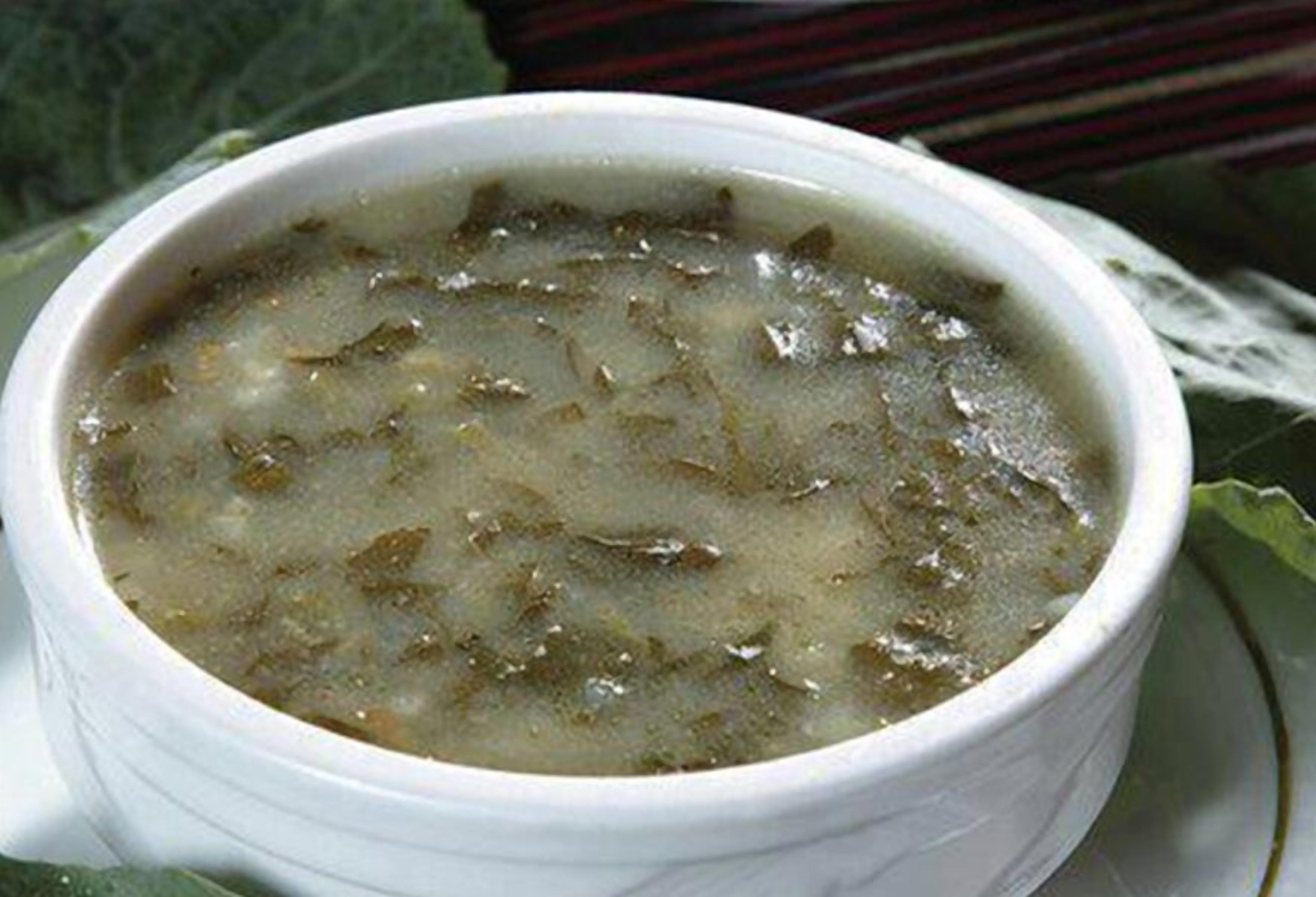 Un tazón de sopa con un interior blanco y un caldo oscuro, servido en un plato blanco adornado con una hoja verde.