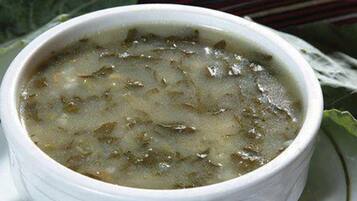 Un tazón de sopa con un interior blanco y un caldo oscuro, servido en un plato blanco adornado con una hoja verde.