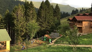 A rustic cabin with a green roof, surrounded by a playground and dense forest. - Hamsiköy Zitaş Otel & Bungalov & Restoran (Maçka)